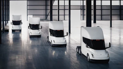 A rendering of four Tesla Semi battery-electric Class 8 trucks parked inside a warehouse.