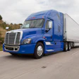 Blue Freightliner semi-truck with silver trailer driving on highway