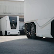 White autonomous truck parked in industrial warehouse facility with commercial vehicles