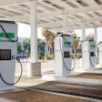 Row of white Greenlands electric vehicle charging stations under a covered canopy with palm trees visible in background