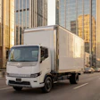 White Harbinger commercial delivery truck driving on urban street with tall buildings