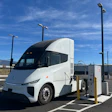 White and black electric semi-truck charging at public charging station under blue sky