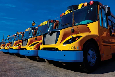 A row of bright yellow Lion Electric school buses lined up in an outdoor parking lot.