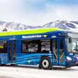 Blue and lime green Mountain Line electric bus parked in snowy mountain landscape