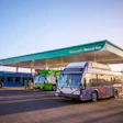 Three public transit buses refueling at a renewable natural gas station under a teal canopy at sunset