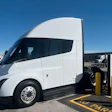 White Tesla Semi truck charging at Tesla Supercharger station in parking lot