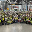 Large group of warehouse workers in safety vests gathered for a team photo in an industrial facility