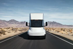 A front-facing view of a white Tesla Semi driving along a desert highway.
