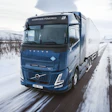 Blue Volvo hydrogen-powered semi-truck driving on snowy winter road with mountains in background