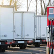 Red and blue electric vehicle charging station with multiple cables in outdoor parking area with trucks in background