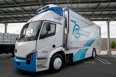 A Lion6 Class 8 battery-electric truck sits parked under a covered structure.