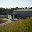 Autonomous delivery robot navigating curved path near industrial warehouse facility surrounded by forest