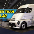 White electric semi-truck on display at trade show with charging stations and blue promotional backdrop