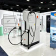 White electric vehicle charging station with dual black cables displayed at trade show booth with branded signage