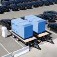 Two blue portable storage boxes on flatbed trailers in a parking lot with black vehicles