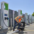 Worker in safety vest servicing electric vehicle charging stations in outdoor lot on sunny day