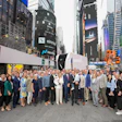 Large group of business professionals posing together in Times Square with tall buildings and digital billboards in the background.