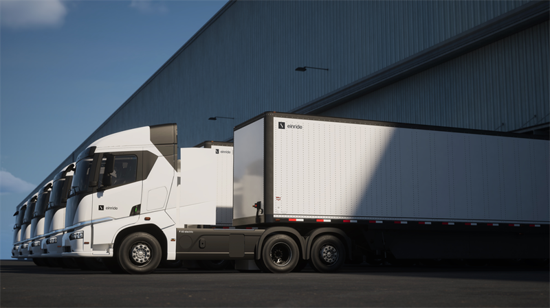 A lineup of Einride battery-electric semis with trailers attached parked at a warehouse loading dock.