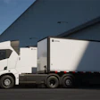 White commercial truck with refrigerated cargo trailer parked outside industrial warehouse facility