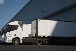 A lineup of Einride battery-electric semis with trailers attached parked at a warehouse loading dock.