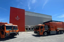 Two orange Mack LR refuse trucks parked outside of a Kingston, Ontario, Canada industrial building.