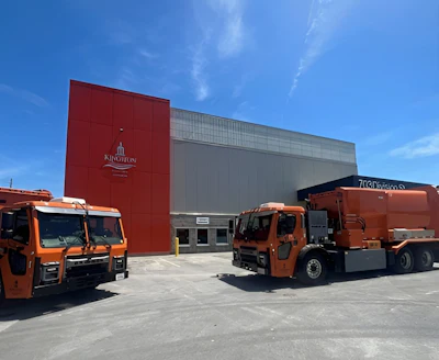 Two orange Mack LR refuse trucks parked outside of a Kingston, Ontario, Canada industrial building.