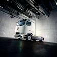 White Mercedes-Benz electric truck parked in modern industrial warehouse with concrete walls and overhead lighting