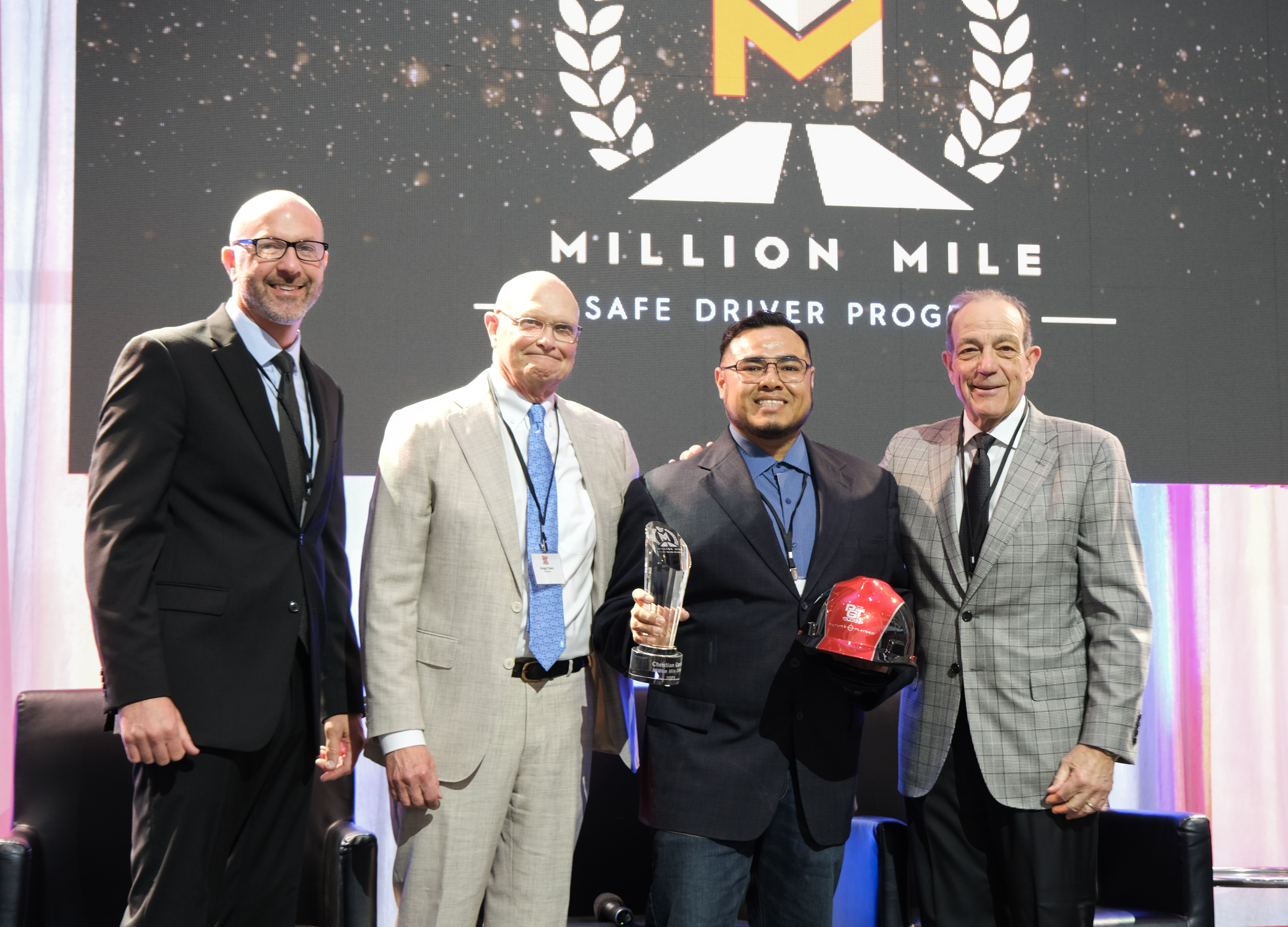 PGT Trucking inducted five new Million Mile Drivers for safe driving in 2025, including Christian Garcia, shown on stage with COO Chad Marsilio, President Gregg Troian and CEO Pat Gallagher.