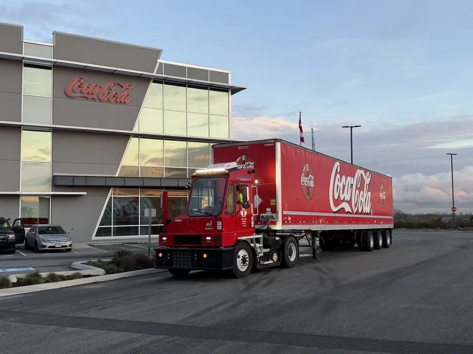 A Coca-Cola-branded Orange EV terminal truck hauling a Coca-Cola trailer outside Coke Canada Bottling's headquarters.