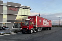 A Coca-Cola-branded Orange EV terminal truck hauling a Coca-Cola trailer outside Coke Canada Bottling's headquarters.