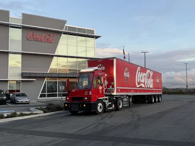 A Coca-Cola-branded Orange EV terminal truck hauling a Coca-Cola trailer outside Coke Canada Bottling's headquarters.