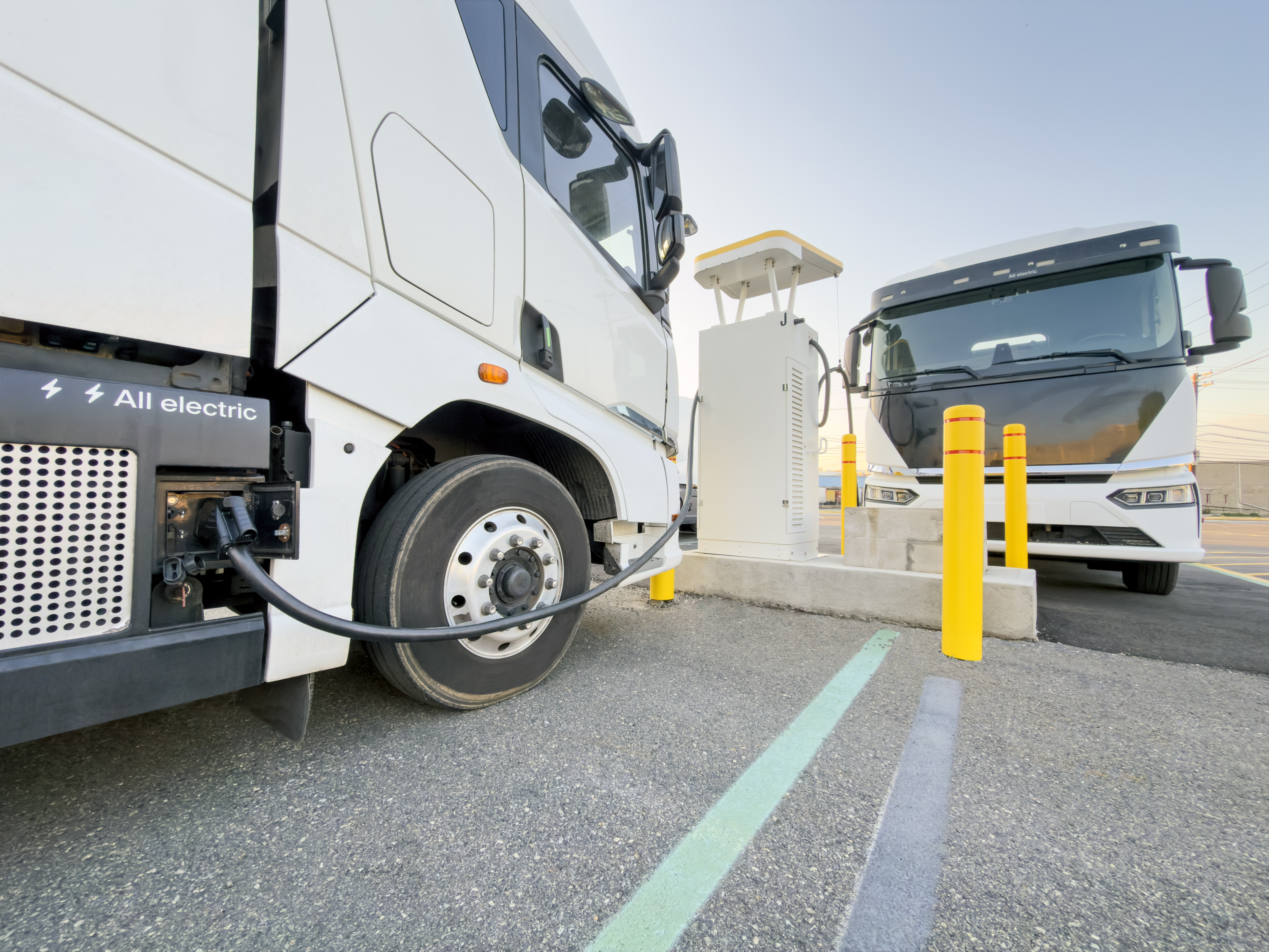 A pair of battery-electric commercial trucks charging at an unknown location.