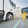Electric trucks charging at public charging station with yellow safety bollards
