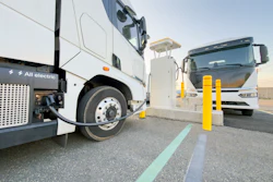 A pair of battery-electric commercial trucks charging at an unknown location.