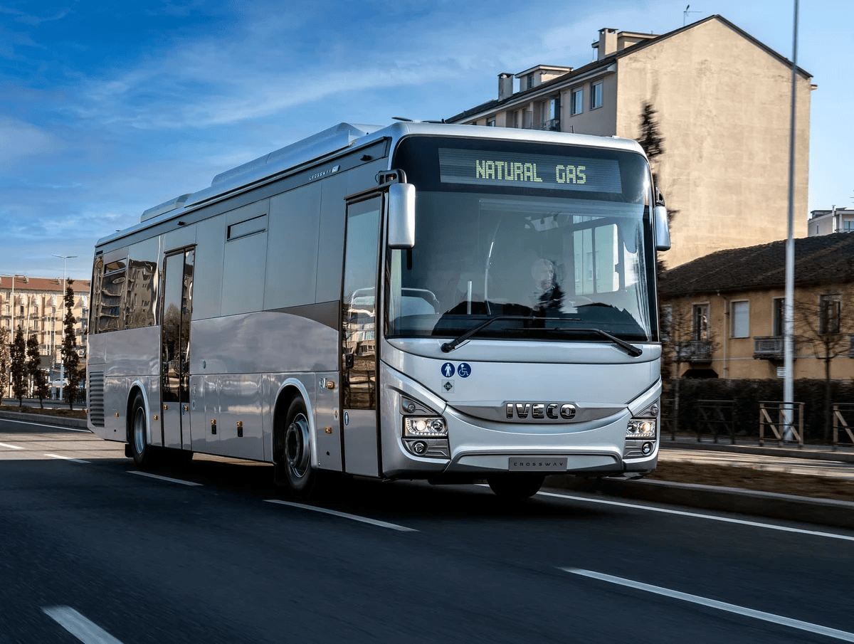 A natural gas-powered IVECO BUS passenger bus travels along an urban street.
