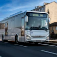 White Iveco natural gas bus driving on urban street with buildings in background