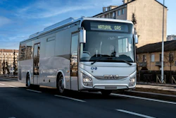 A natural gas-powered IVECO BUS passenger bus travels along an urban street.