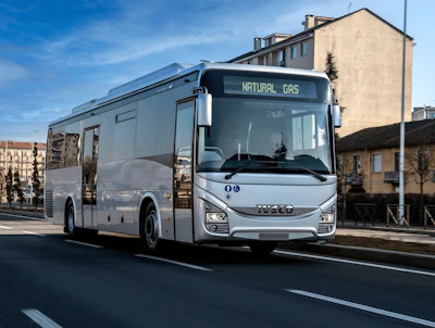 A natural gas-powered IVECO BUS passenger bus travels along an urban street.