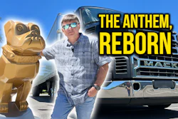 Man in sunglasses and plaid shirt posing with golden Mack bulldog statue and Mack truck under blue sky