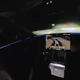Nighttime vehicle interior view with illuminated dashboard, blue accent lighting, and forward-facing camera display showing road ahead