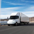 White Tesla Cybertruck semi-truck driving on highway with desert landscape and blue sky