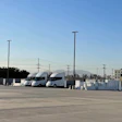 Two white semi-trucks parked in an industrial lot with utility poles and buildings under clear blue sky