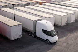 A Tesla Semi with a trailer is parked in a logistics yard alongside other trucks.