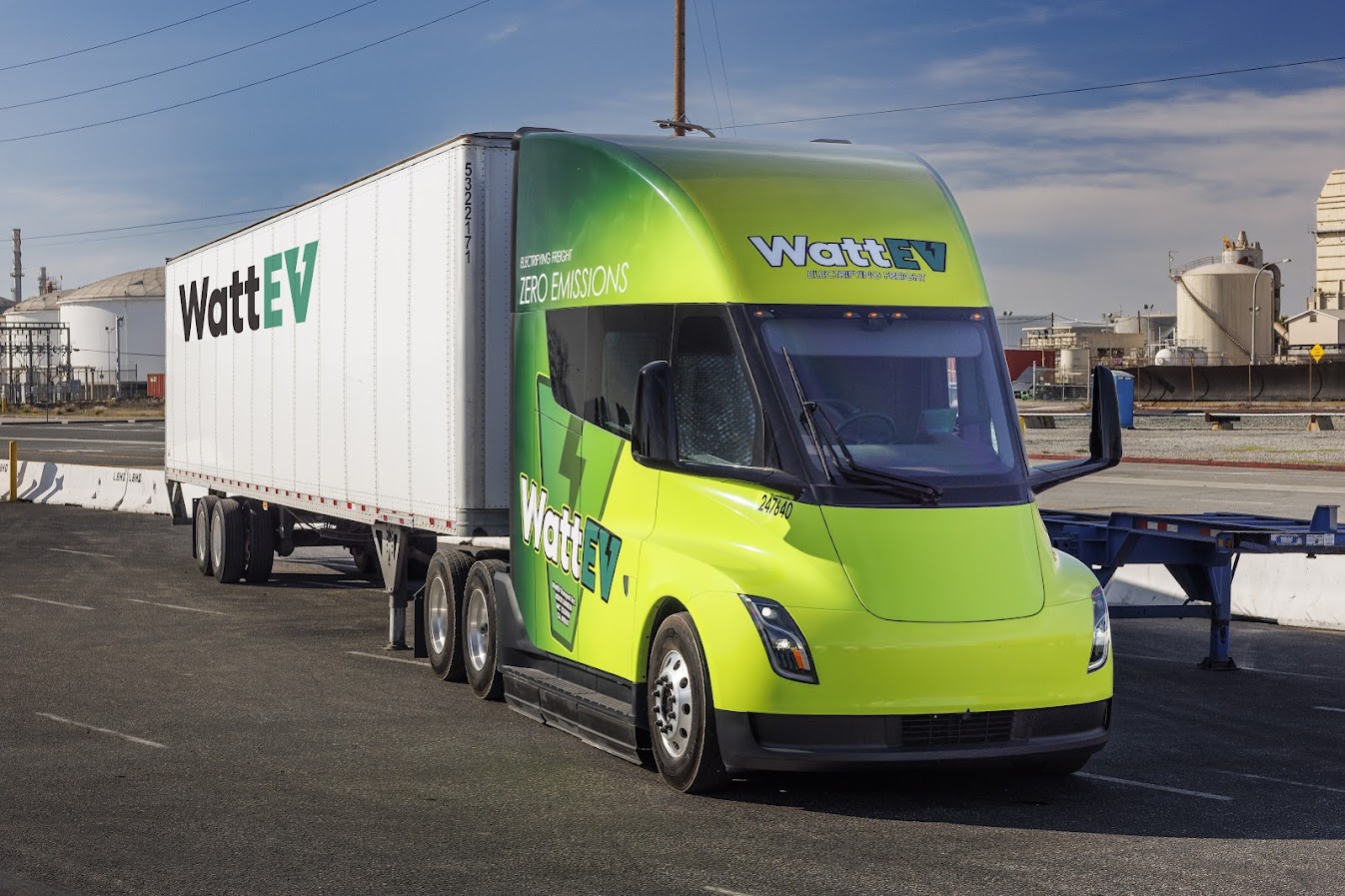 A green and yellow WattEV branded Tesla Semi and trailer parked at an industrial facility.