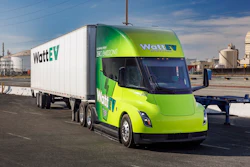 A green and yellow WattEV branded Tesla Semi and trailer parked at an industrial facility.