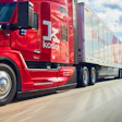 Red Kodiak semi-truck with refrigerated trailer driving on highway under blue sky