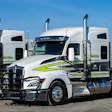 Two white and lime green semi-trucks with trailers loaded with stacked materials at a logistics facility