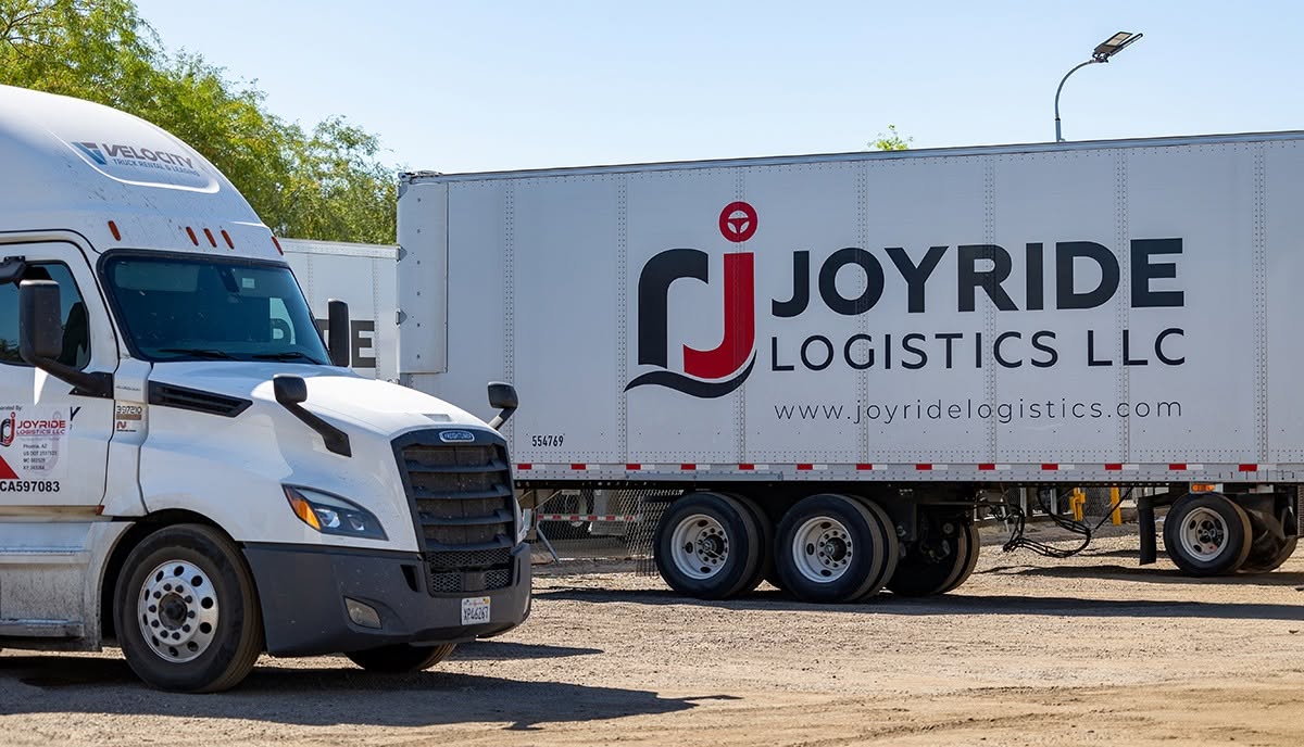 White commercial truck and Joyride Logistics LLC branded trailer parked at logistics facility
