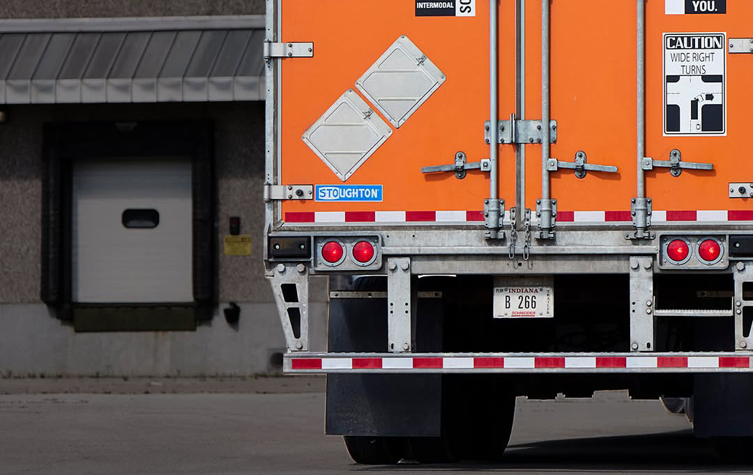 Orange and white International flatbed truck backed up to loading dock with caution sign visible