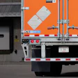 Orange and white International flatbed truck backed up to loading dock with caution sign visible